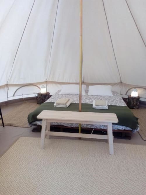 Interior espaçoso da tenda de glamping em Monte da Tojeirinha com banco branco, camas e vista para o lago em Montargil