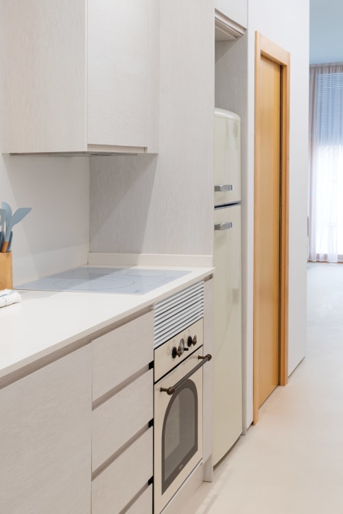 Cocina moderna en apartamento de Gandía con muebles blancos, horno de acero inoxidable y puerta de entrada de madera