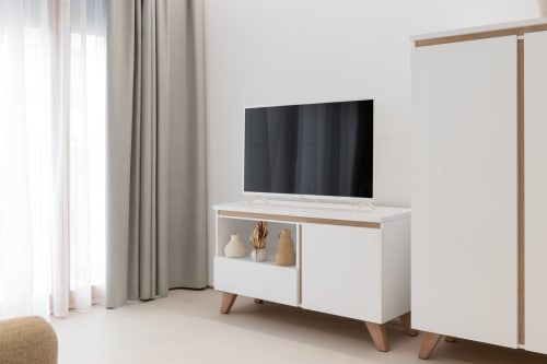 Moderno soporte TV blanco con detalles de madera en luminoso apartamento de Gandía con vistas a la piscina, TV de pantalla plana y diseño minimalista