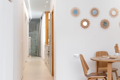 Comedor moderno con mesa y sillas de madera, espejos tejidos decorativos en pared blanca, apartamento en Gandía