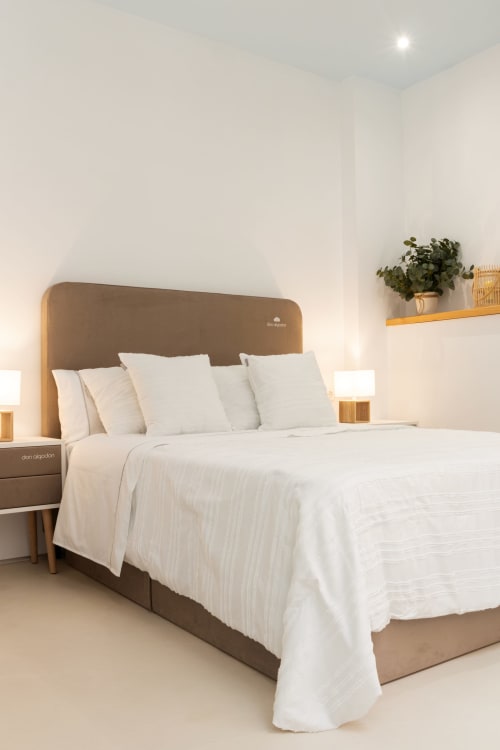 Dormitorio moderno en Ona vacaciones de Gandía con cabecero marrón, ropa de cama blanca, mesitas de madera y decoración con plantas