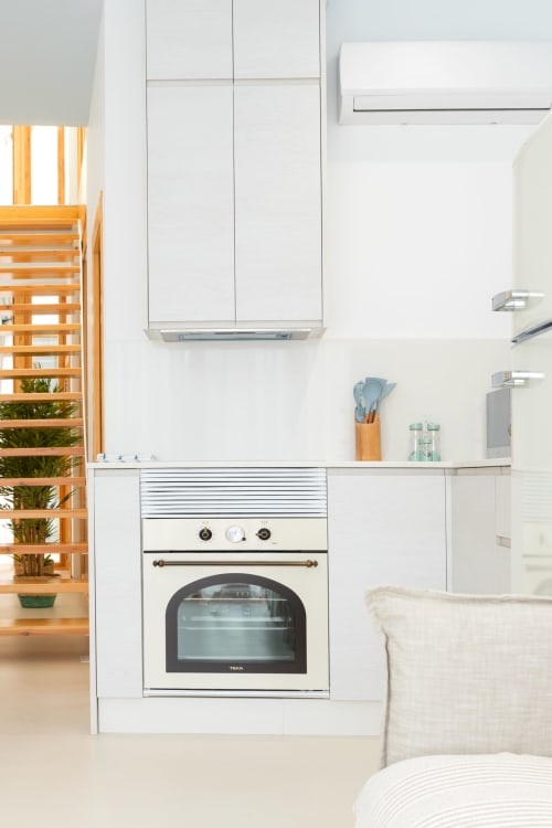 Cocina moderna con muebles blancos, horno integrado y detalles de madera en dúplex de Gandía