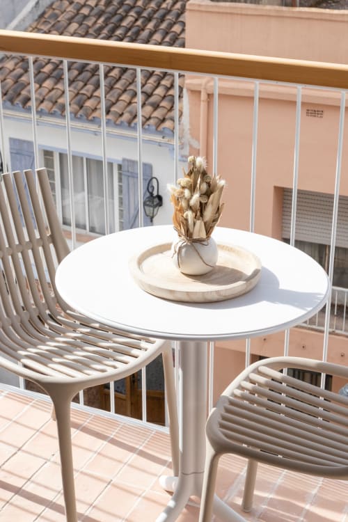 Balcón soleado en Ona vacaciones Gandía con mesa redonda blanca, sillas modernas y flores secas con vistas a la piscina