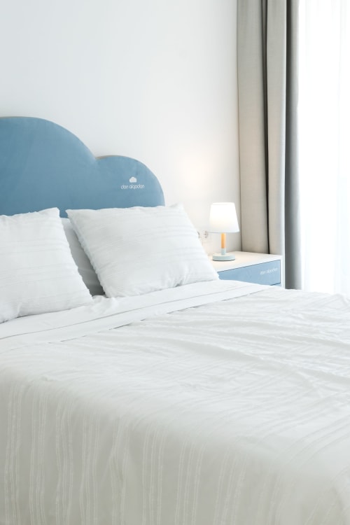 Dormitorio moderno en Ona vacaciones Gandía con cabecero nube azul, almohadas blancas y vista a la piscina desde la lámpara de mesita.