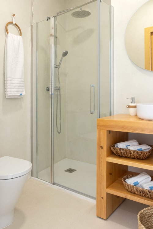 Baño moderno en dúplex de Gandía con cabina de ducha cristalina, tocador de madera y toallas blancas en Ona vacaciones