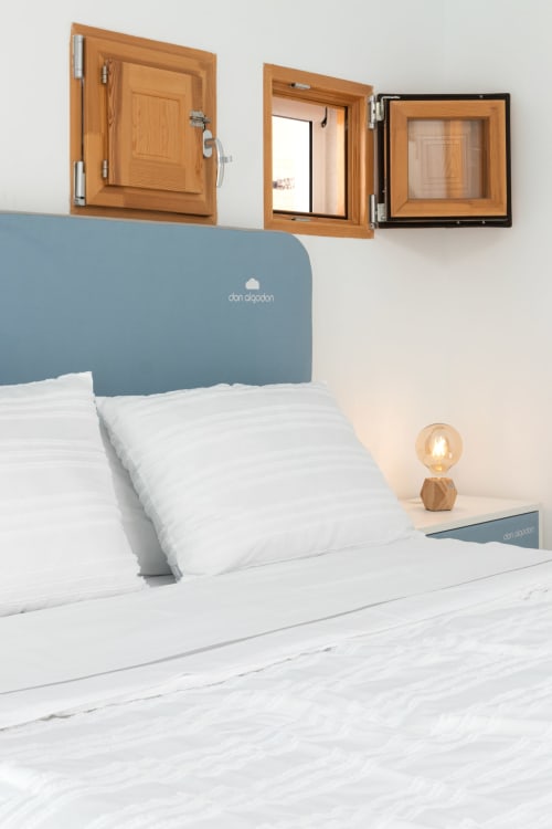 Dormitorio moderno en Ona vacaciones Gandía con ventanas de madera, cabecero azul, ropa de cama blanca e iluminación cálida