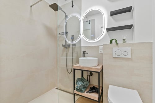 Modern bathroom in Mattbnb's Metz hotel with dual LED mirrors, white vessel sink, rainfall shower, and black metal vanity