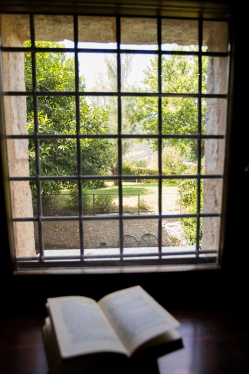 Libro aperto sul davanzale di Le Mura Rooms a Norcia, affacciato su un rigoglioso giardino con alberi verdi