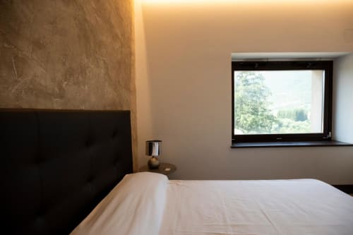 Camera moderna a Le Mura Rooms a Norcia con letto bianco, testata nera, parete in rilievo e vista dalla finestra