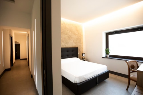 Camera moderna a Le Mura Rooms a Norcia con letto nero, biancheria bianca, illuminazione soft e scrivania di lavoro