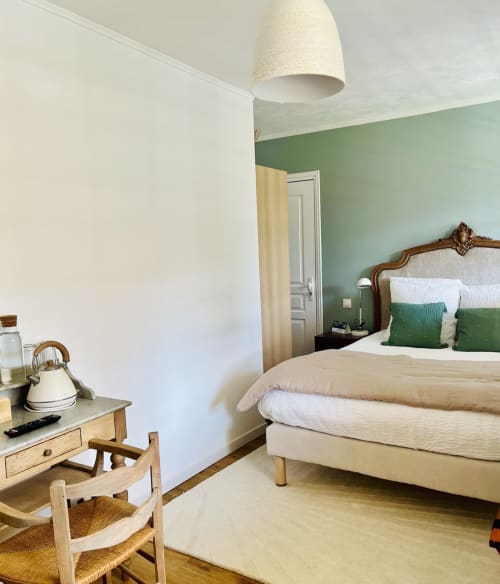 Cosy double bedroom at Le Clos Normand with sage green accent wall, wooden furniture, and garden views