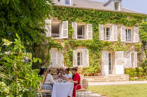 Des clients savourent leur déjeuner sur la terrasse du jardin du Domaine by A&G, une charmante maison vendéenne à façade en pierre couverte de lierre