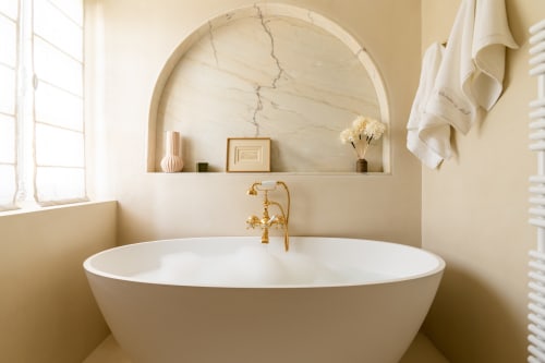 Salle de bains élégante de style spa avec baignoire blanche indépendante, robinetterie dorée et niche en marbre au Domaine by A&G