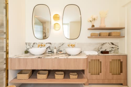 Salle de bains luxueuse avec double vasque en marbre, miroirs ronds, vasques blanches, meubles en bois et paniers de rangement tressés