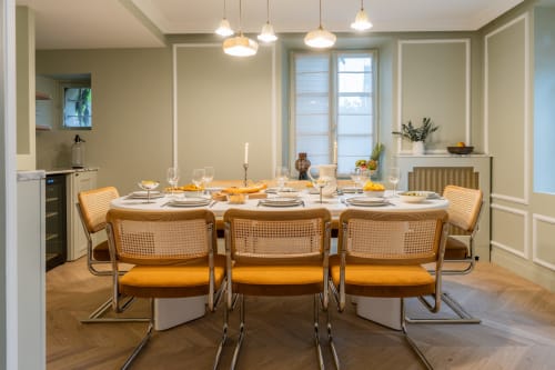 Salle à manger élégante du domaine by A&G Vendrest avec chaises en rotin, couverts blancs et luminaires suspendus