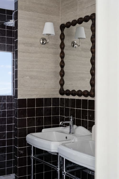 Salle de bain moderne de la villa DEAUV HILLS avec carrelage noir, lavabo blanc, miroir encadré de bois foncé et appliques murales