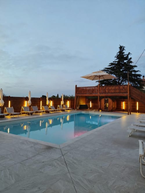 Piscina illuminata del Queen Hotel al tramonto a Campofilone con lettini, ombrelloni e edifici con terrazza in legno