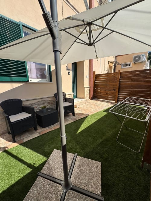 Patio esterno dell'appartamento Queen Hotel Anastasia a Campofilone, con ombrellone a sbalzo, lettino nero e arredi artificiali