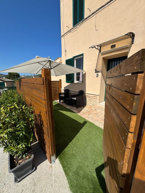 Terrazza dell'appartamento Queen Hotel Anastasia a Campofilone con recinzione in legno, ombrellone, sedute e prato artificiale
