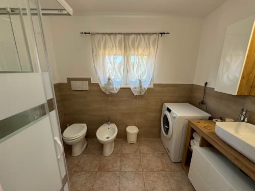 Bagno spazioso nell'appartamento Anastasia dell'Hotel Queen, Campofilone, con toilette, bidet, lavatrice e finiture in legno