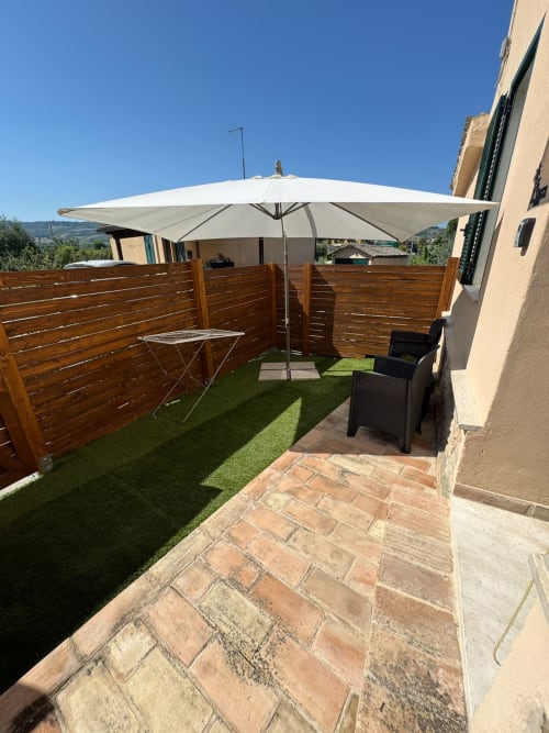 Patio ombreggiato dell'hotel Queen a Campofilone con recinzione in legno, ombrellone e sedia nera con vista sulla campagna