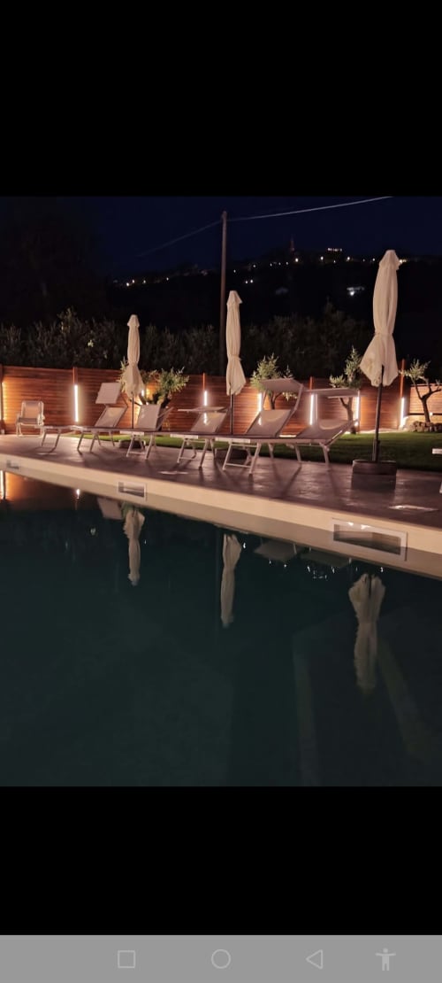 Patio a bordo piscina di notte al Queen Hotel di Campofilone con lettini, ombrelloni e luci ambientali riflesse nell'