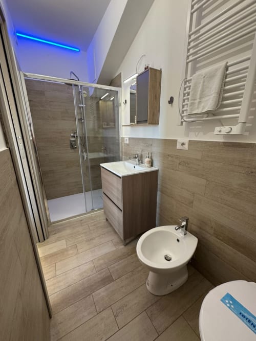 Bagno moderno della stanza Sissi al Queen Hotel di Campofilone con doccia walk-in, mobile in legno, bidet e illuminazione blu