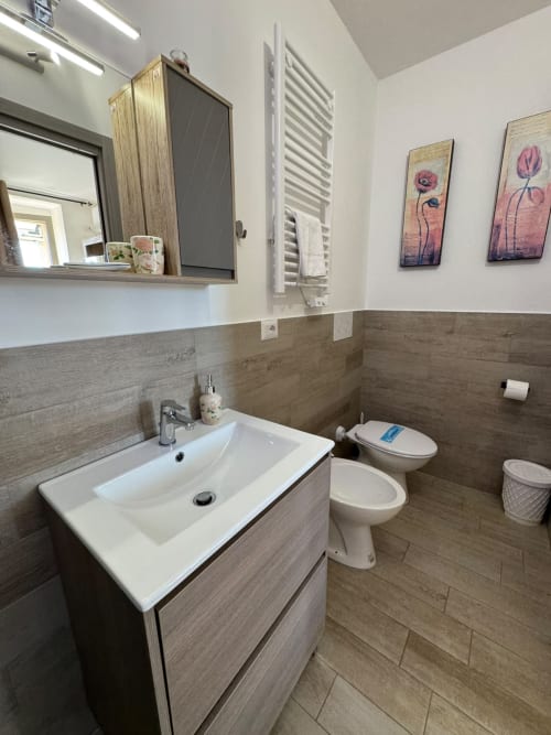 Bagno moderno nella camera Sissi dell'hotel Queen a Campofilone, con lavabo, toilette e opere floreali