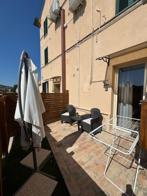 Soleggiato patio della camera Sissi del Queen Hotel a Campofilone con sedute, ombrellone e pavimenti in cotto