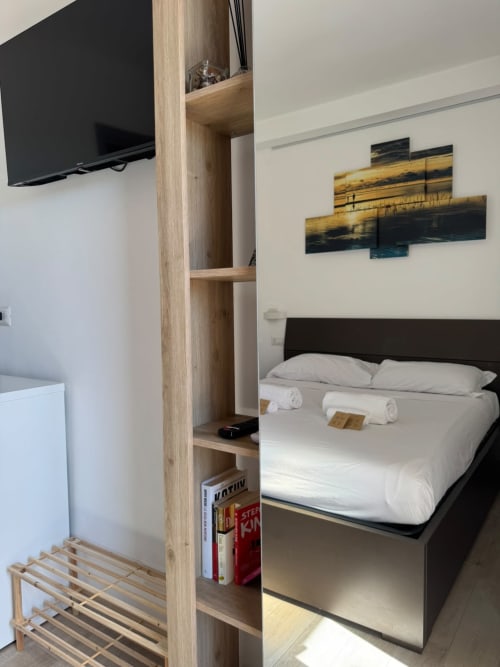Camera d'albergo moderna a Campofilone con TV a schermo piatto, letto nero, biancheria bianca, scaffalature in legno e quadri paesaggistici