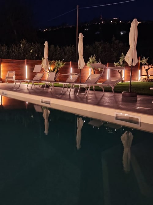 Vista notturna della piscina illuminata del Queen Hotel Campofilone con lettini, ombrelloni e luci paesaggistiche
