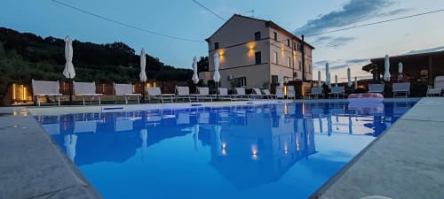 Piscina dell'Hotel Queen al tramonto a Campofilone con edificio illuminato, lettini, ombrelloni e verde circostante