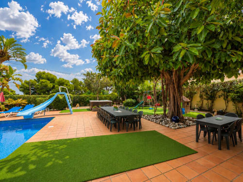 Patio de la villa Casa Emilia en Moraira con piscina, mesas de comedor, árbol frondoso y jardín impecable