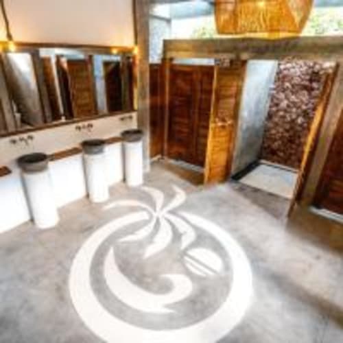 Female dormitory bathroom at Kaniu Lombok Hostel in Kuta with white vanities, wooden flooring, and decorative tile pattern