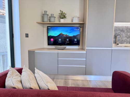 Salon moderne avec canapé bourgogne, téléviseur mural affichant des paysages montagneux, étagère en bois décorée et rangements gris