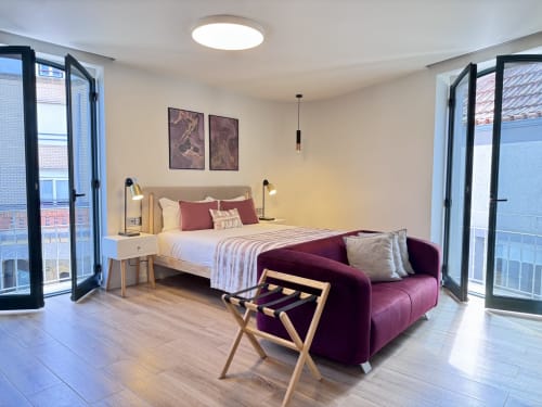 Chambre moderne au RIA CENTRUM Smart Residence à Aveiro avec lit queen-size, canapé violet et vue sur la ville depuis les balcons
