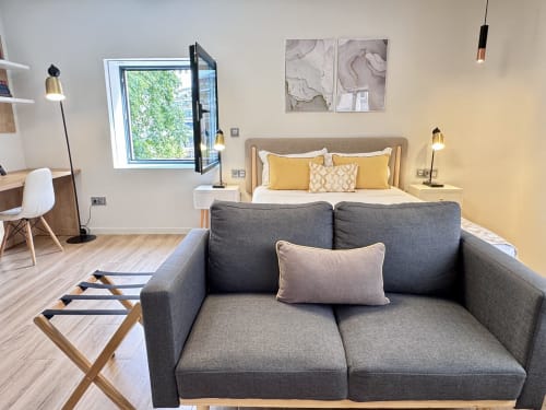 Quarto moderno com sofá cinza, detalhes em amarelo e vista para a cidade na RIA CENTRUM Smart Residence, Aveiro