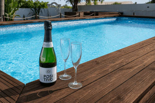 Champagne bottle and glasses on wooden deck beside sparkling blue pool at Quinta do Águas villa, Lagoa Portugal