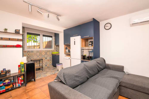 Acogedora sala de estar moderna con sofá gris, cocina abierta, refrigerador blanco, salpicadero decorativo y piso de terracota