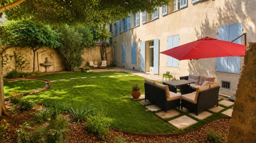 Les Suites de Montigny courtyard with lush green lawn, red umbrella, seating area, and stone building in Aix-en-Provence