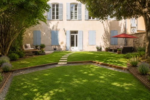 Lush garden courtyard at Les Suites de Montigny, Aix-en-Provence, featuring manicured lawn, shaded seating areas, and elegant