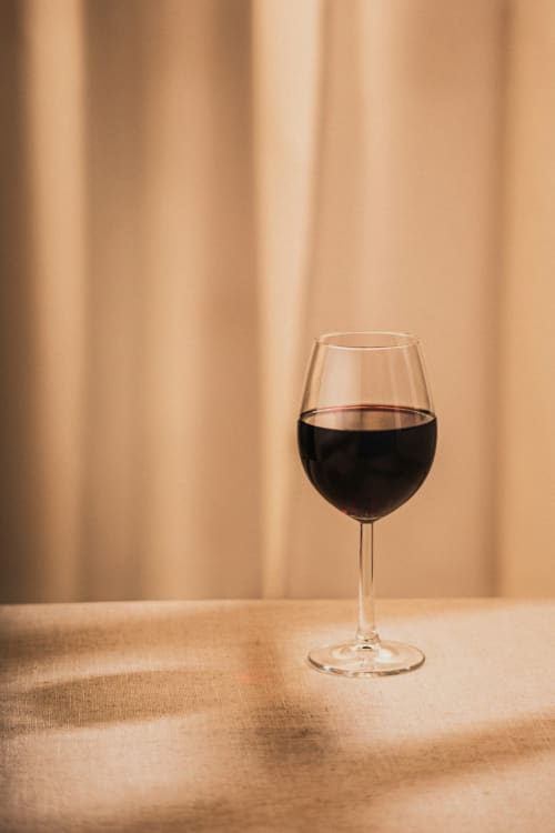 Verre de vin rouge sur table beige avec rideaux au Château du Landin, chambre d'hôtes française
