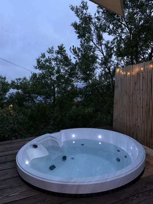 Illuminated round hot tub on wooden deck at Agritusmo Stecadò in Dolceacqua with garden views and evening ambiance