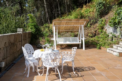Zona de comedor al aire libre en la casita Vilaboa de Pontevedra con sillas metálicas blancas, mesa y columpio de pérgola con vistas a la montaña