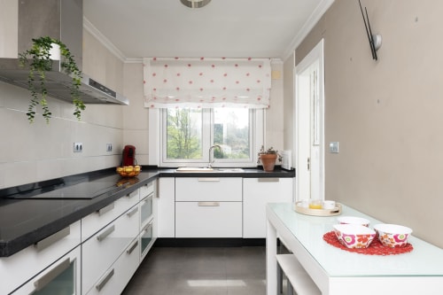 Cocina moderna blanca con encimeras negras, electrodomésticos de acero inoxidable y vistas a las montañas en la casa rural Vilaboa de Pontevedra
