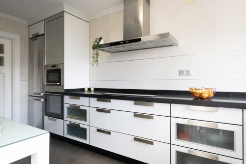 Cocina moderna con muebles blancos, encimera negra, electrodomésticos de acero inoxidable y campana extractora en la casita de Vilaboa
