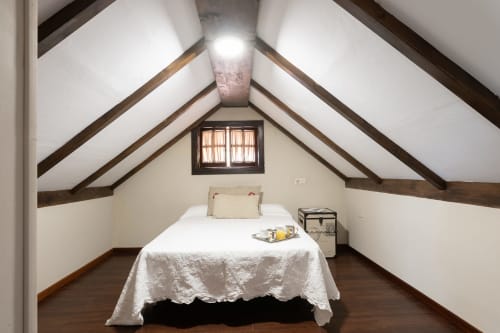 Acogedor dormitorio abuhardillado en la casita de Vilaboa cerca de Pontevedra con vigas de madera vista, ropa blanca y vistas a la montaña