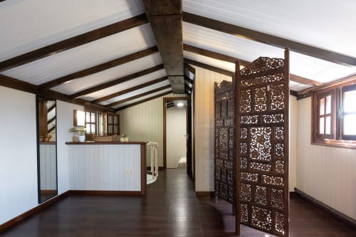 Sala de estar diáfana en casita con vigas de madera, suelo oscuro, biombo decorativo y ventanales en Pontevedra