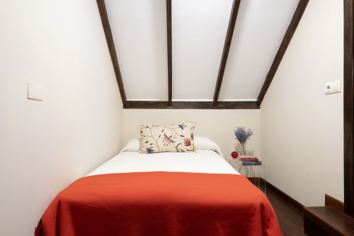 Acogedora habitación con manta roja, almohada decorativa y vigas de madera vistas en la casita rural Vilaboa de Pontevedra