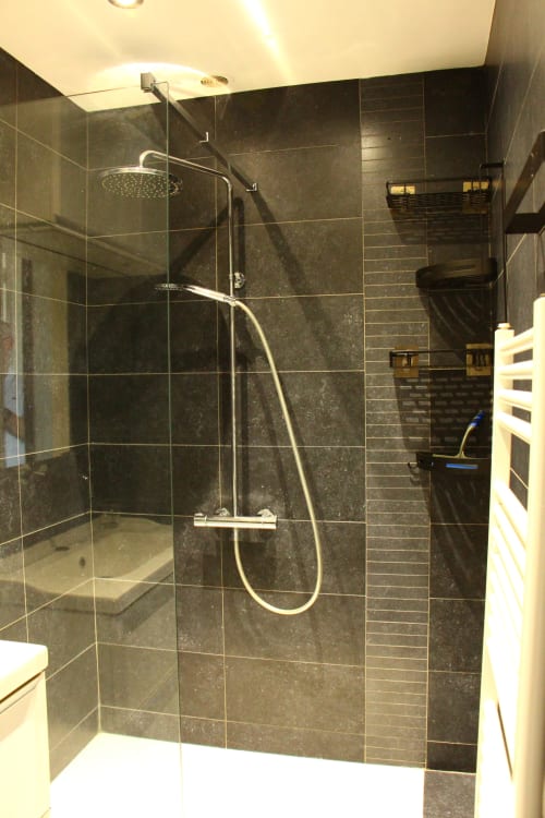 Modern walk-in shower with dark tile walls and glass enclosure at Le Cardinal apartment in Reims, France